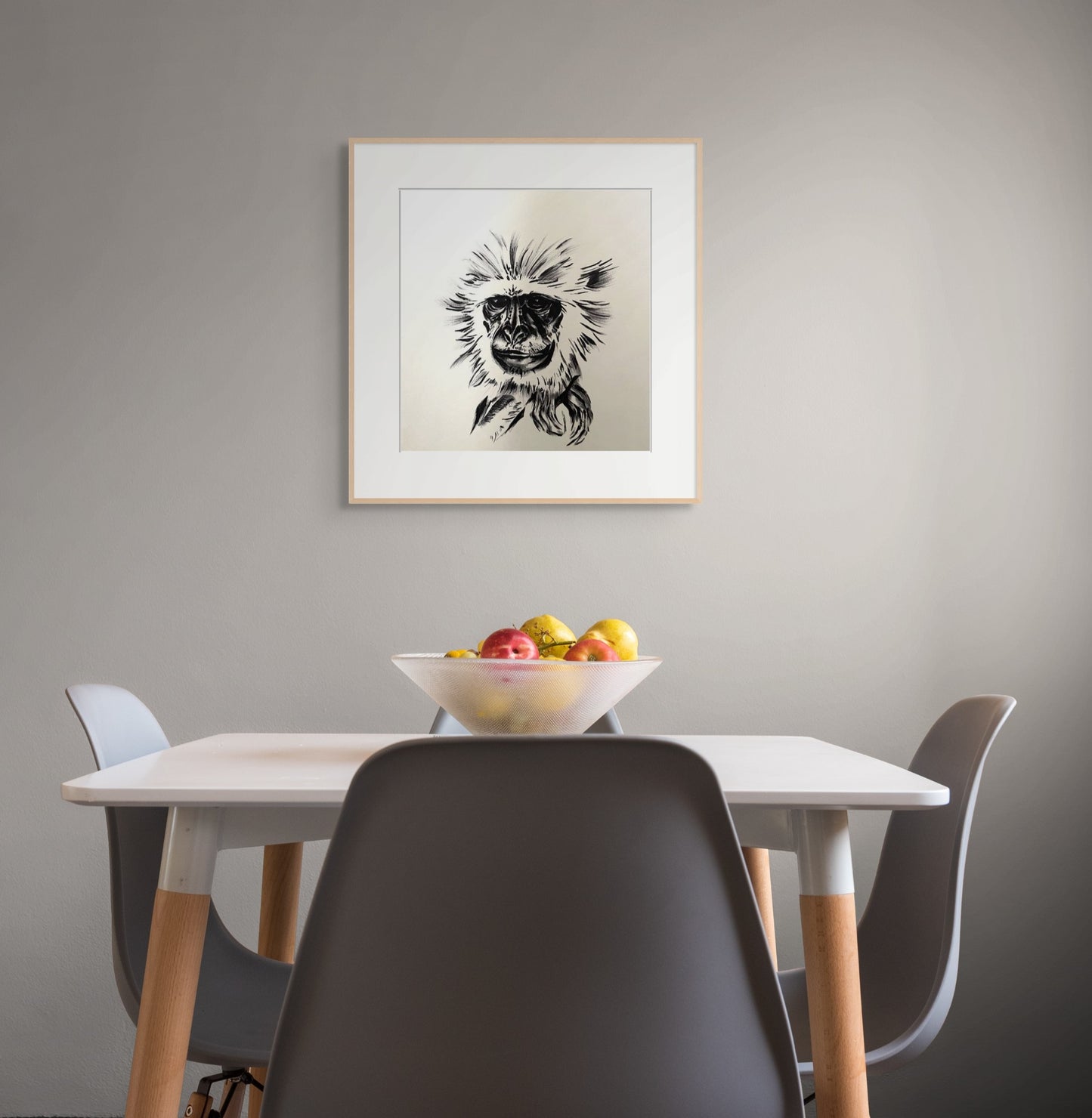 Framed pen drawing of a Vervet Monkey hangs above a dining table with a bowl of fruit.