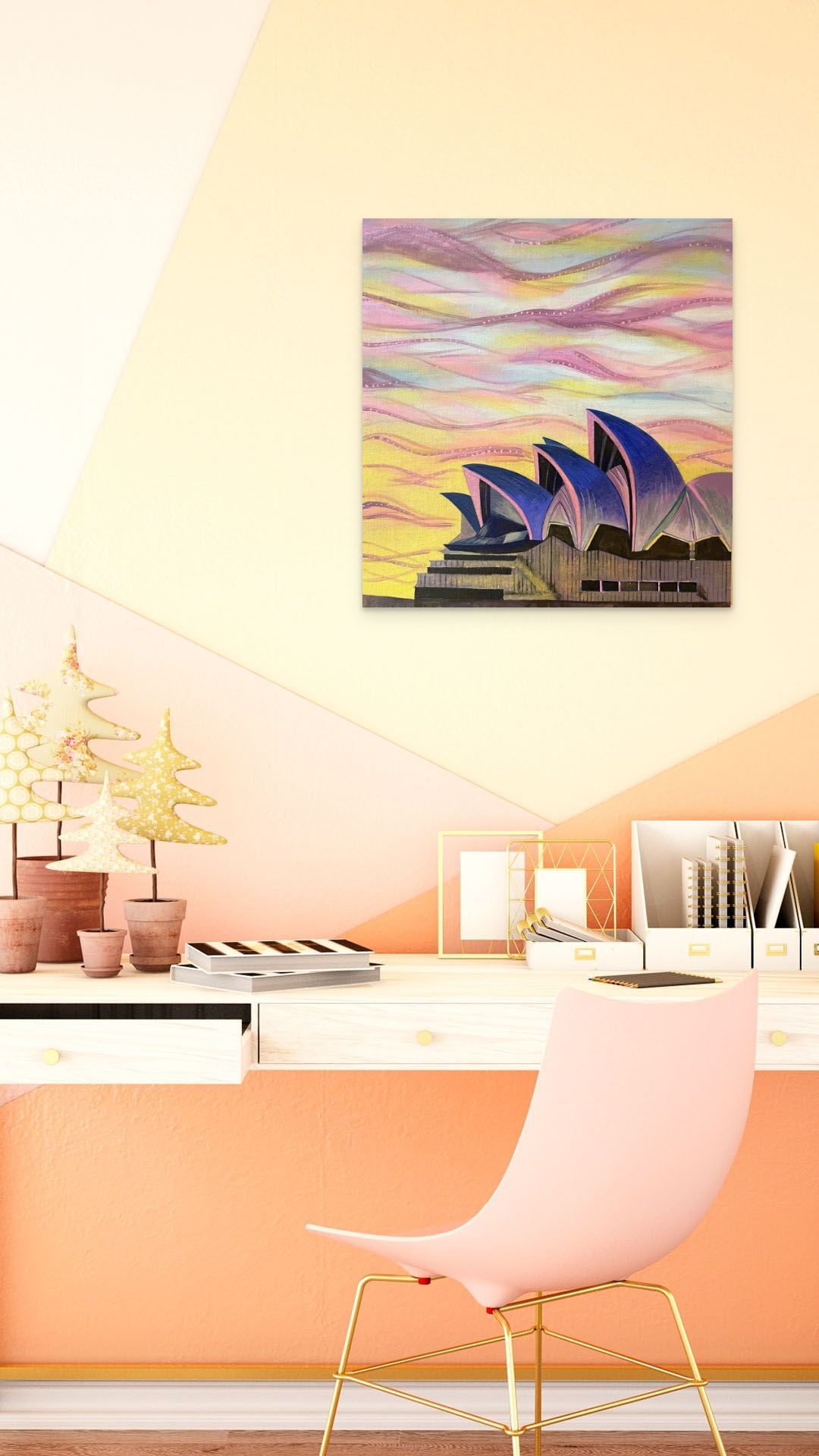 Painting of the Opera House at sunset hanging above a desk with pink and gold accessories.