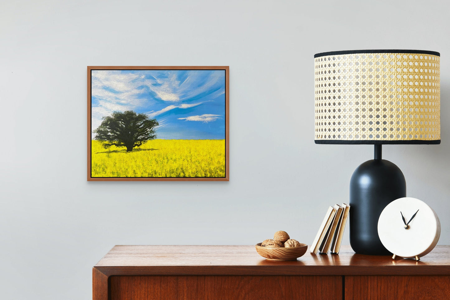 Painting on canvas of a canola field above a cherry wood cabinet with a black lamp