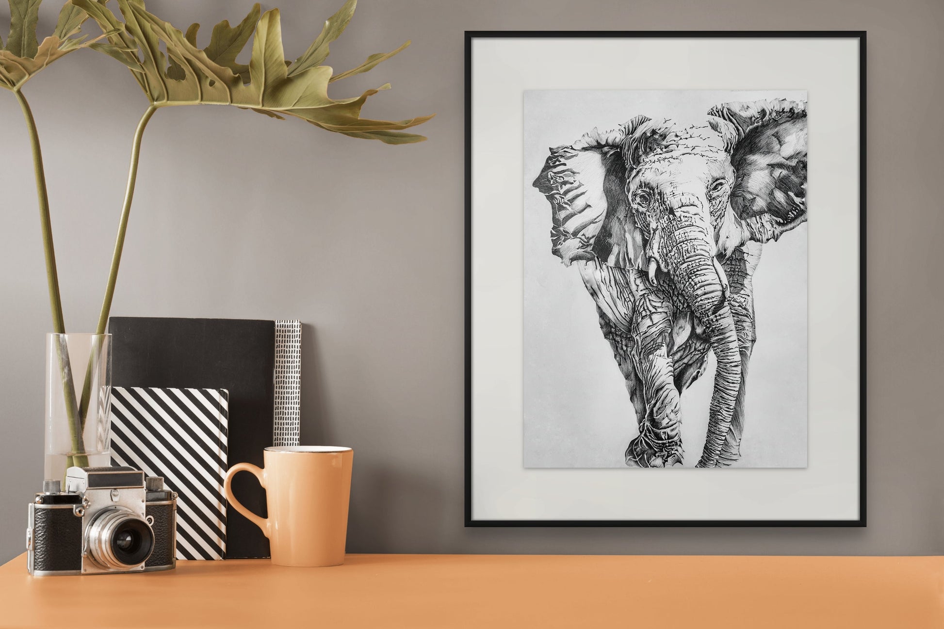 Pencil drawing of an elephant hanging above a safari camera on a peach table.