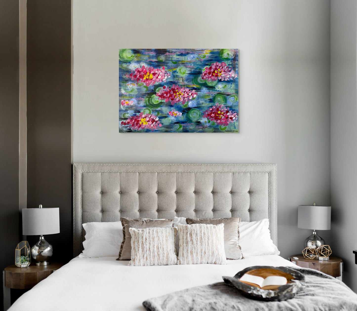 A framed painting of pink lilies in a pond hanging in a luxurious bedroom.