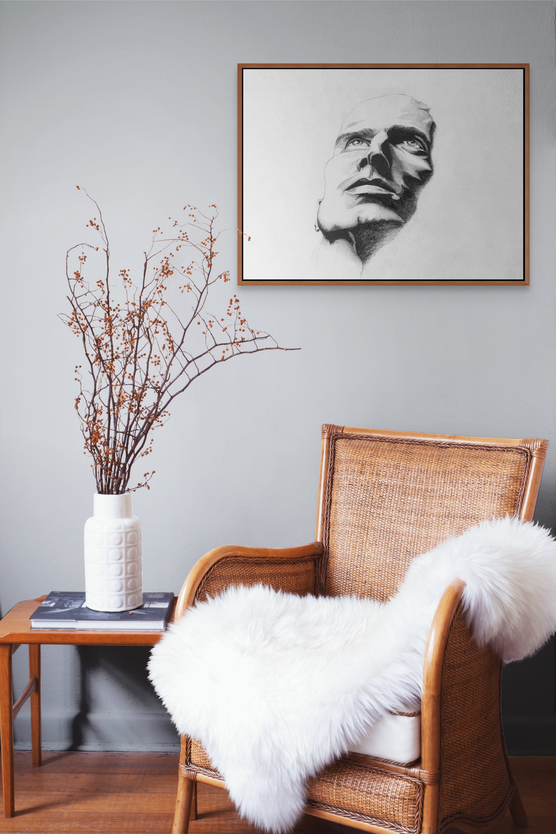 Framed black & white pencil sketch hanging above a wicker chair with a fluffy throw blanket. man looking up.