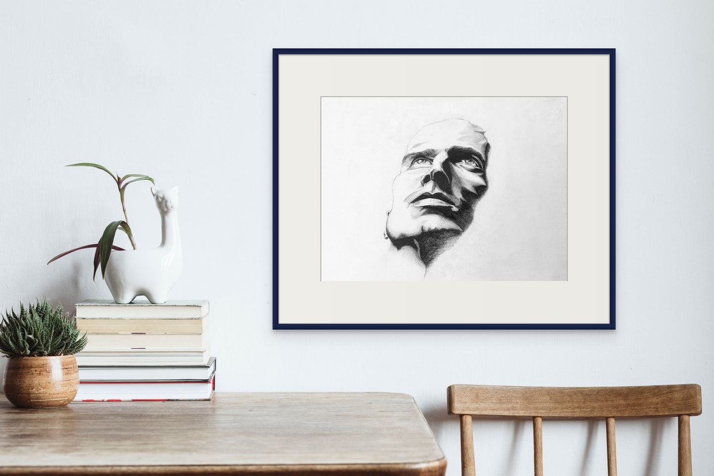 Framed black & white pencil sketch hanging above a wooden table. Sketch shows a man looking up. 