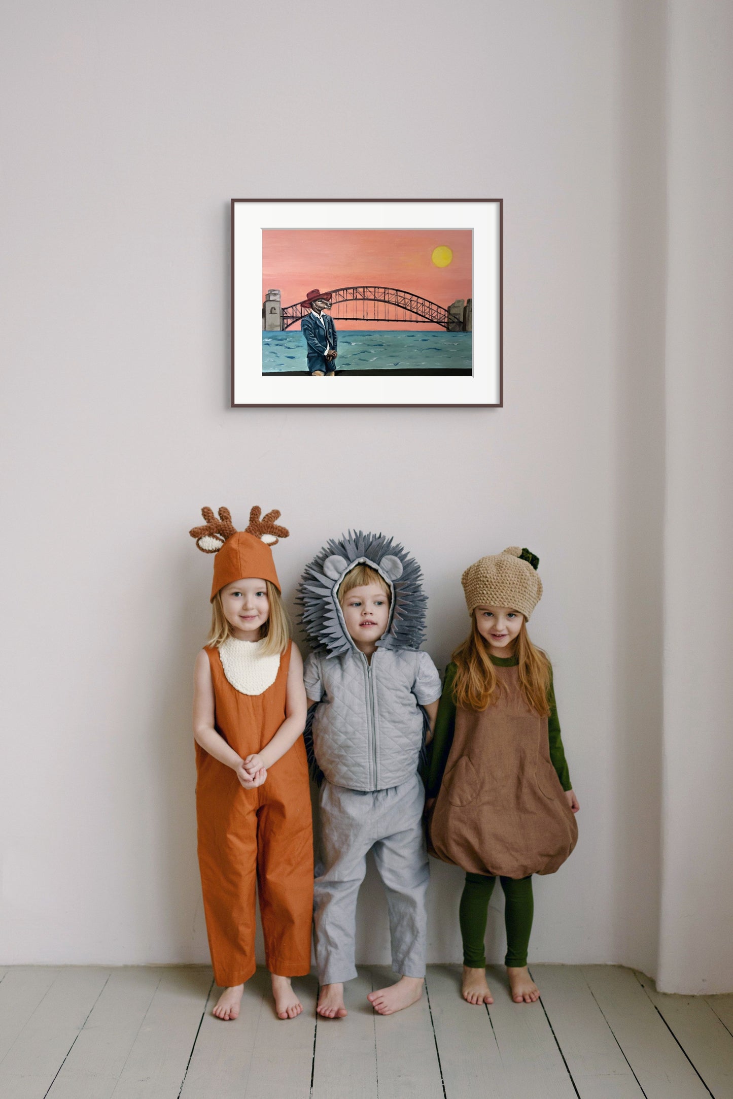 Framed painting of a kangaroo in a suit standing in front of the Sydney Harbour Bridge, hanging above three children in dress up costumes.