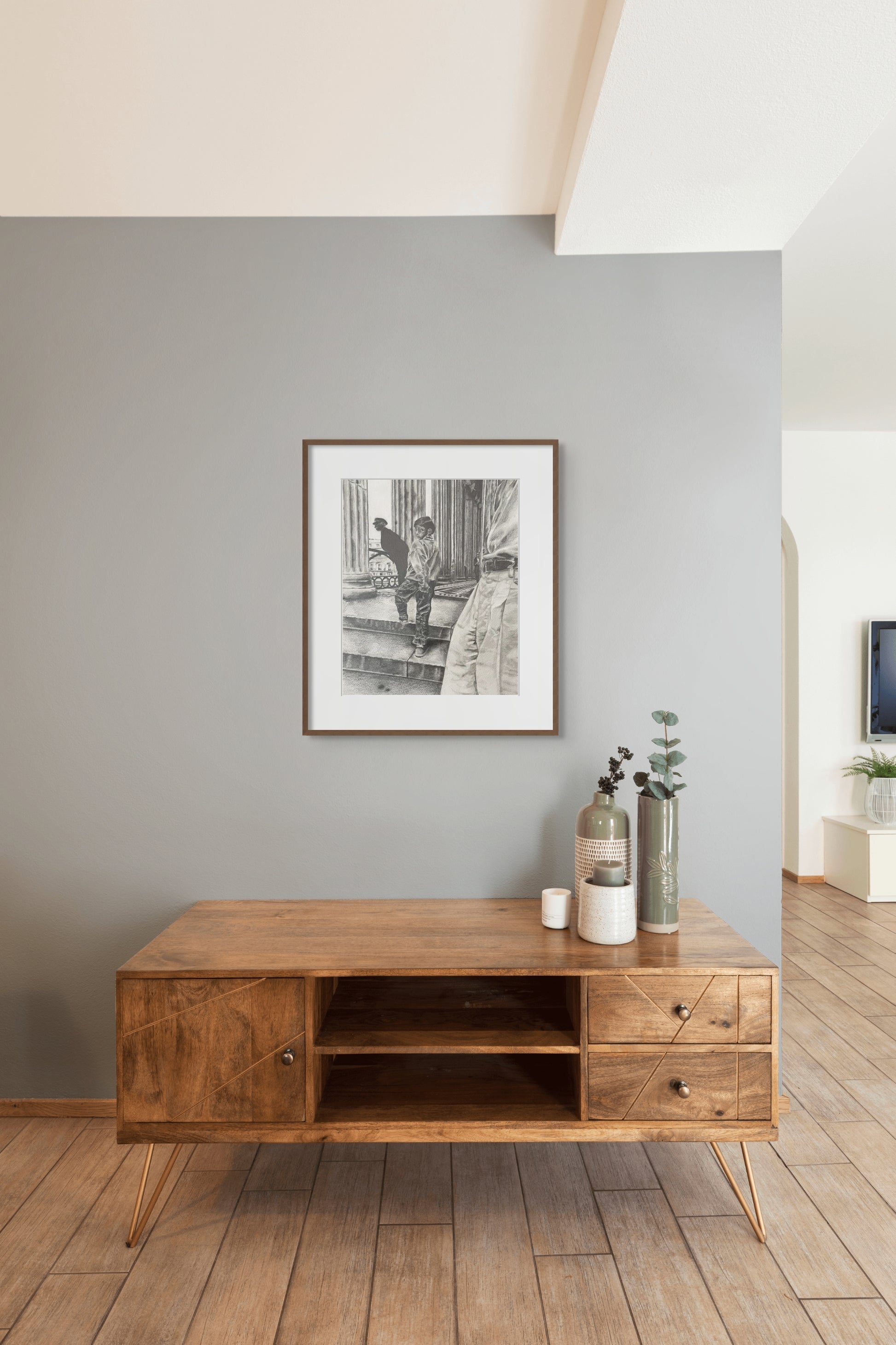 A framed drawing of a boy walking up the stairs to a museum hangs above a wooden cabinet.