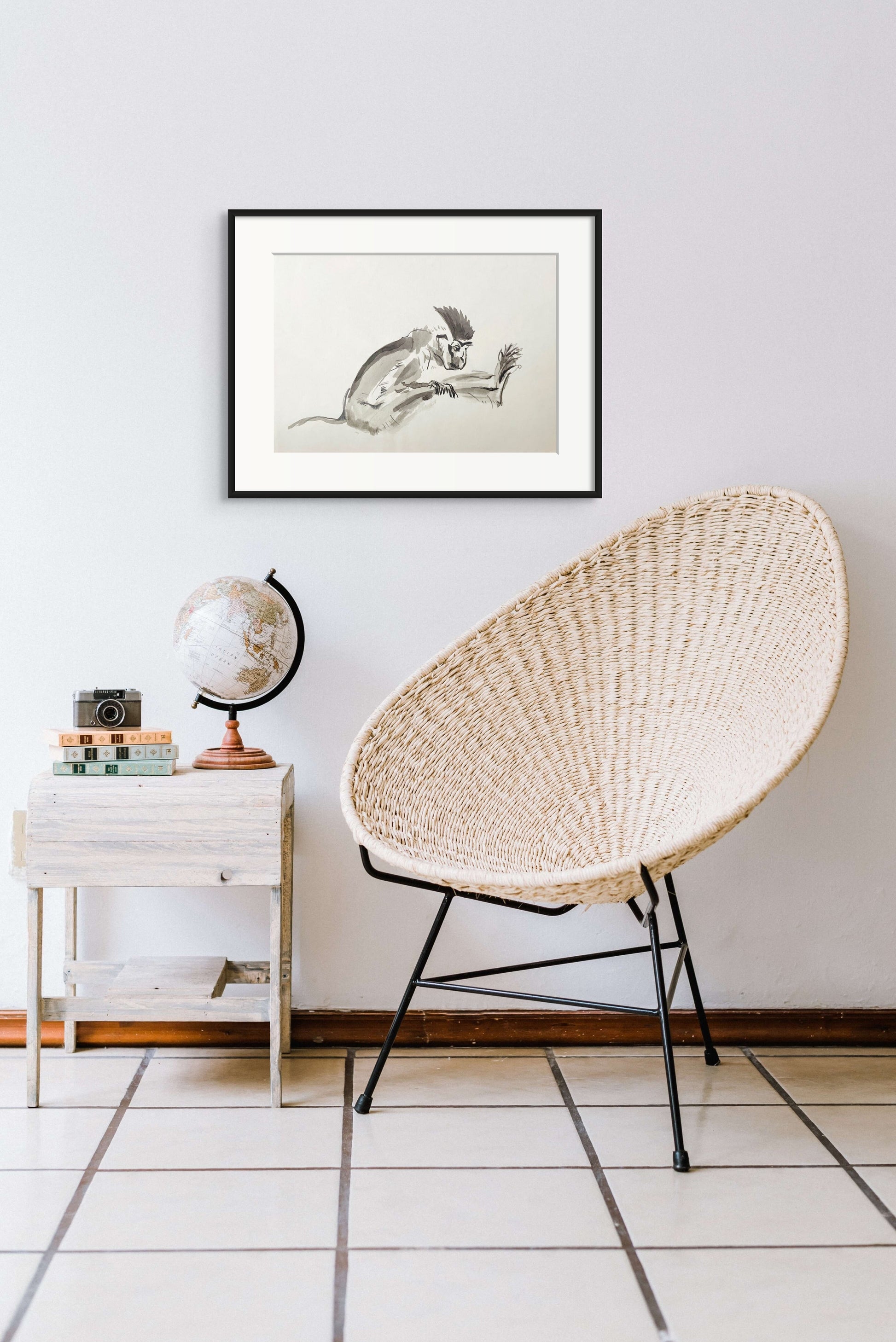 Greyscale painting of an African Vervet Monkey hanging on a white wall above a chair and table.